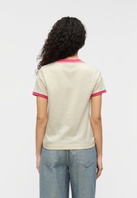 Κρεμ μπλουζάκι με κοντά, ροζ περιμετρικά μανίκια και ανάλογο λαιμόκοψη. Απαλή ύφανση με άνετη εφαρμογή, συνδυασμένο με τζιν ανοιχτού μπλε.