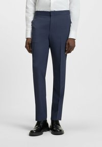 Pantaloni blu navy con una vestibilità sartoriale, caratterizzati da una texture liscia e una piega pressata, abbinati a scarpe stringate nere.