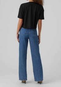Czarny krótki t-shirt z krótkimi rękawami w połączeniu z wysokim stanem niebieskich dżinsów i czarnych szpilek, pokazany od tyłu.