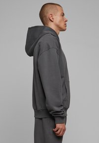 Felpa grigia con cappuccio, dal taglio rilassato, texture morbida, tasca a marsupio e polsini a coste, progettata per comfort e abbigliamento casual.
