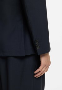 Granatowa marynarka o gładkiej fakturze, z kołnierzem z wycięciem, czterema czarnymi guzikami na mankiecie oraz dopasowanym krojem.