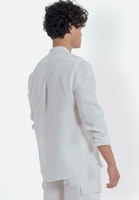 Witte linnen blouse met lange mouwen, zichtbare knoopdetails, opgerolde manchetten en een afgeronde zoom. Zachte textuur, lichtgewicht ontwerp.