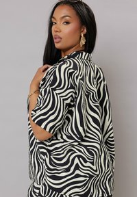 T-shirt med zebramönster som har svarta och krämvitt vågiga ränder, korta ärmar och en avslappnad passform. Tyget verkar lätt och texturerat.