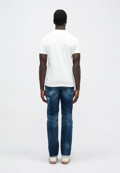 Weißes T-Shirt mit kurzen Ärmeln kombiniert mit blauen Jeans. Das T-Shirt hat einen klassischen Schnitt, die Jeans sind leicht abgenutzt, mit geradem Schnitt und Taschen.