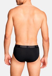 Schwarze Herrenbody mit passgenauer Passform, ausgestattet mit einem matten, gerippten Bund, der das Puma-Logo in Schwarz zeigt. Glatte Textur und schlichtes Design.