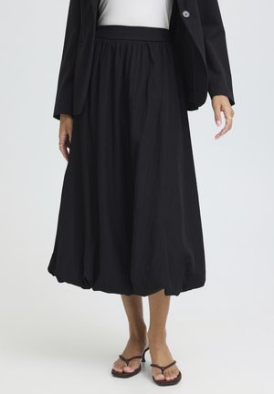 Pantaloni neri a gamba ampia e taglio corto con orli arricciati, indossati con blazer nero, top bianco e sandali con tacco marroni su una modella.