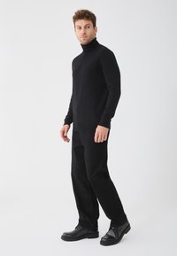 Pulover negru cu guler înalt asortat cu pantaloni negri drepti și pantofi negri cu șireturi. Textură netedă, design ajustat și schemă de culori monocromă.