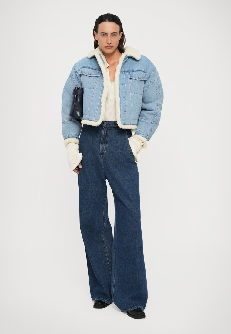 Veste en denim bleu clair coupée avec doublure en shearling, associée à un jean large taille haute noir et des chaussures noires ; design simple, look décontracté.