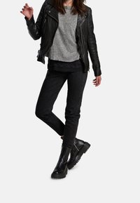 Svart läderbikerjacka över en grå T-shirt, parat med svarta skinny jeans och svarta kraftiga stövlar; en avslappnad lager-på-lager-outfit.