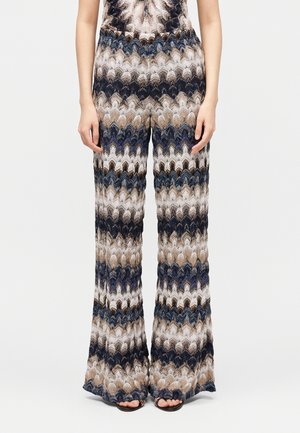 Donna che indossa pantaloni a vita alta e gamba larga con un motivo lavorato a maglia ondulato multicolore nelle tonalità del blu, beige, marrone e bianco.