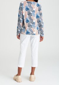 Top leggero a maniche lunghe con un motivo astratto multicolore nei toni del blu, pesco e nero, abbinato a pantaloni bianchi a gamba affusolata e scarpe chunky color beige.