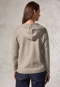 Ljusgrå stickad hoodie med ett strukturerat mönster på ärmarna, ribbade muddar och midja. Har en justerbar huva och en avslappnad passform.