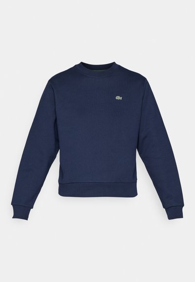 Sweatshirt bleu marine en tissu doux, avec un col rond et des poignets côtelés. Petit logo vert Lacoste sur la poitrine.