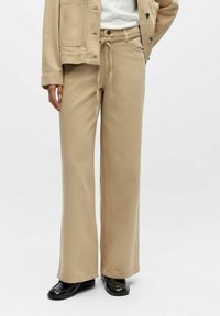 Bēšas krāsas platām kājām bikses no mīksta auduma, ar auklu regulējamu jostasvietu, diskrētām sānu kabatām un gludu, vienkāršu virsmu.