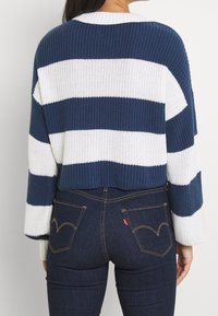 Pull en maille avec des rayures horizontales bleu marine et blanches, présentant une texture côtelée et un col rond, porté avec un jean denim foncé.