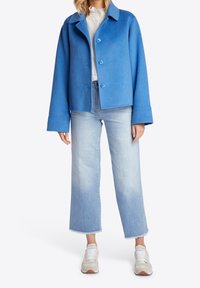 Blå filtjakke med krave og knapper foran, kombineret med lyseblå, korte jeans og beige sneakers med hvide snørebånd.