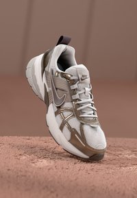 Nike-Sneaker mit einem weißen Mesh-Obermaterial, braunen Akzenten und einer strukturierten Sohle. Enthält einen gepolsterten Kragen und ein sichtbares Schnürsystem.