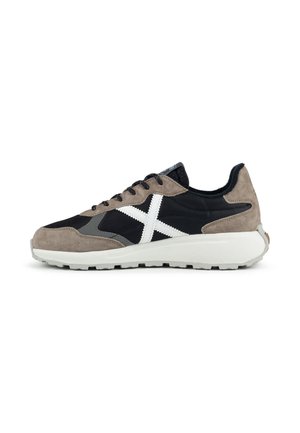 Zapatilla baja con tejido negro, superposiciones de ante gris, suela blanca, cordones negros y una gran X blanca cosida en el lateral.
