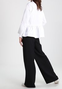Blusa peplum bianca con maniche lunghe abbinata a pantaloni neri a palazzo. Tessuto morbido con vestibilità rilassata; design semplice senza pattern visibili.