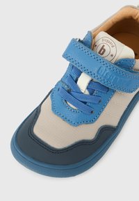 Παιδικό αθλητικό παπούτσι σε μπλε και μπεζ χρώμα με λουράκι βέλκρο, μπλε κορδόνια και ετικέτα της μάρκας στη γλώσσα που γράφει "bisgaard".