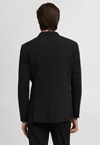 Jachetă neagră din suit cu o croială ajustată, rever în formă de v și mansete cu nasturi, având o textură de țesătură netedă și un design simplu, curat.