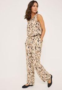 Ensemble deux pièces beige avec un haut sans manches et un pantalon large, orné d'un motif de feuilles noir et brun. Tissu doux avec une coupe décontractée.