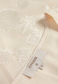 Gros plan sur un tissu de couleur crème avec une broderie florale et une étiquette cousue indiquant "cream 38" près de la couture.