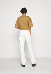 Camiseta castanha cropped com mangas curtas, combinada com jeans brancos de perna reta de cintura alta. Botas pretas robustas. Fundo minimalista.