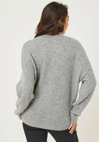 Ljusgrå, överdimensionerad tröja i mjukt, fluffigt material med ribbad nederkant och lösa ärmar. Baksidan har en enkel design.