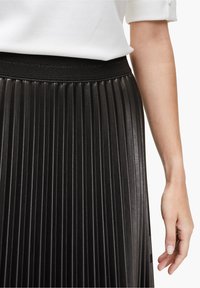 Falda negra plisada hecha de cuero sintético con una cinturilla elástica negra texturizada, que presenta rayas verticales y un brillo suave.