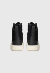 Chaussures montantes noires en suède et cuir, avec une doublure en fausse fourrure douce au col et une semelle en caoutchouc blanc. Fermeture éclair sur les côtés.