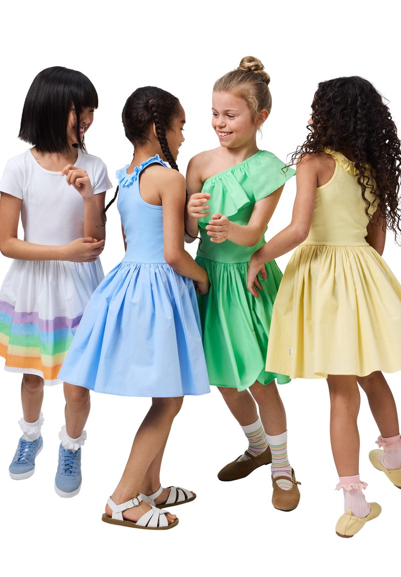 Τέσσερα παιδιά με πολύχρωμα φορέματα: λευκό με ουράνιες γραμμές, μπλε με βολάν, πράσινο με έναν ώμο και κίτρινο, συνδυασμένα με ποικιλόμορφα υποδήματα.