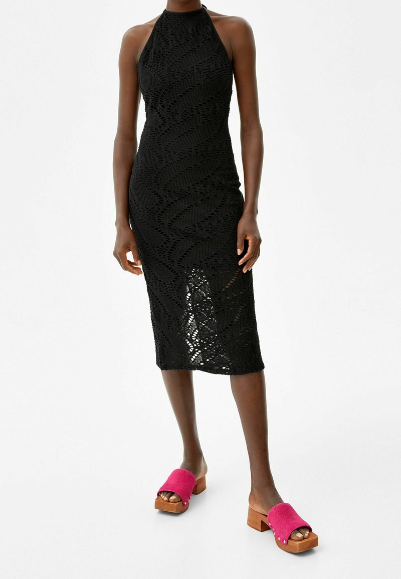 Robe midi noire en crochet coupe slim avec col bateau, associée à des sandales à plateforme en bois avec des lanières rose vif.