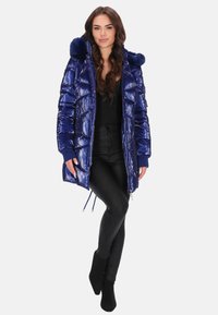 Sötétkék pufi kabát fényes felülettel, bolyhos kapucnival és bordázott mandzsettákkal. Cipzárral és állítható húzózsinórokkal ellátott, hogy a méret tökéletes legyen.