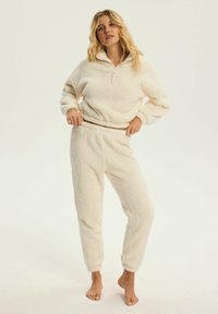 Miękki komplet dresowy z materiału futrzanego, składaj ący się z rozpinanej bluzki z wykładanym kołnierzem i spodni z elastycznym pasem, oba z mankietami i ściągaczami na kostkach.