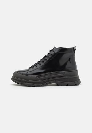 Botte montante noire à lacets avec semelle en caoutchouc épaisse et languette à l'arrière, vue de profil extérieur sur fond blanc.