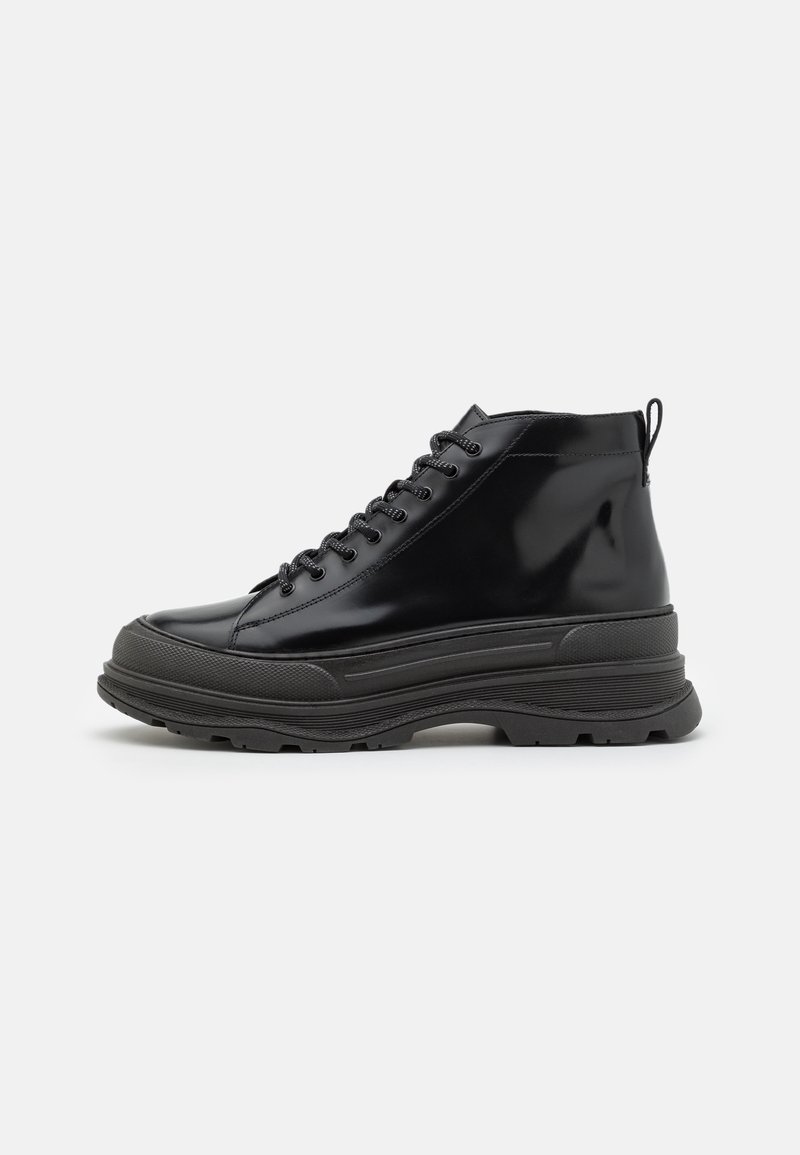 Botte montante noire à lacets avec semelle en caoutchouc épaisse et languette à l'arrière, vue de profil extérieur sur fond blanc.