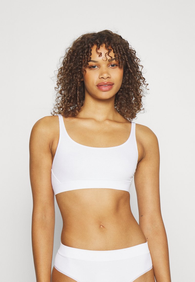 Bralette blanco de algodón con tirantes finos, escote redondeado y una banda elástica ancha en la parte inferior. Textura suave y elástica.