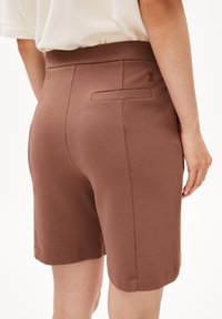 Bruine stretchshorts met een gladde textuur, een medium hoge taille en een achterzak. Bevat decoratieve steken en een klein embleem nabij de taille.