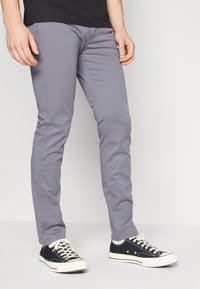 Grijze katoenen broek met slim fit, gecombineerd met zwarte canvas sneakers. De broek heeft een soepele textuur en subtiele stikseldetails.