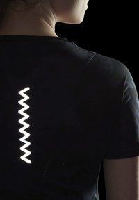 Camiseta atlética negra con un diseño reflectante en zigzag en la parte posterior, que resalta su textura suave y su forma ajustada. No se ven más detalles.