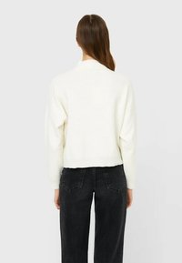 Witte cropped sweater met een geribbelde zoom en verlaagde schouders, gecombineerd met zwarte high-waisted jeans met achterzakken en een rechte pasvorm.