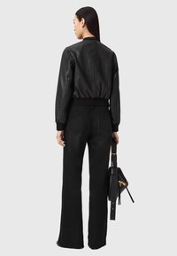 Sort læder bomberjakke med elastisk taljebånd, kombineret med højtaljede sorte flare-jeans. Modellen holder en sort håndtaske med gulddetaljer.