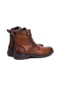 Botas de cuero marrón hasta el tobillo con un acabado suave, cremallera lateral y parte delantera con cordones, que presentan un tirador de talón en contraste y detalles de costura.