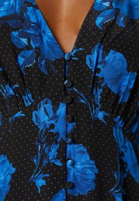 Robe noire à petits pois blancs et grands motifs floraux bleus, avec des boutons recouverts de tissu sur le devant.