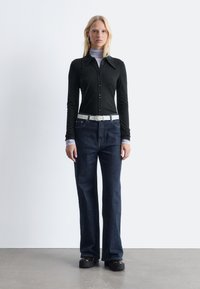 Long-sleeve black button-up shirt with a collar, paired with dark blue wide-leg jeans and a white belt. Model wears platform shoes.