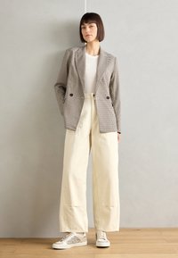 Blazer à carreaux beige et noir, associé à un pantalon large crème. Les chaussures sont des baskets beiges avec des accents pailletés.