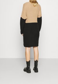 Stickad klänning i beige och svart, med avslappnad passform, långa ärmar och ribbad struktur, stylad med svart ankellång stövlar.