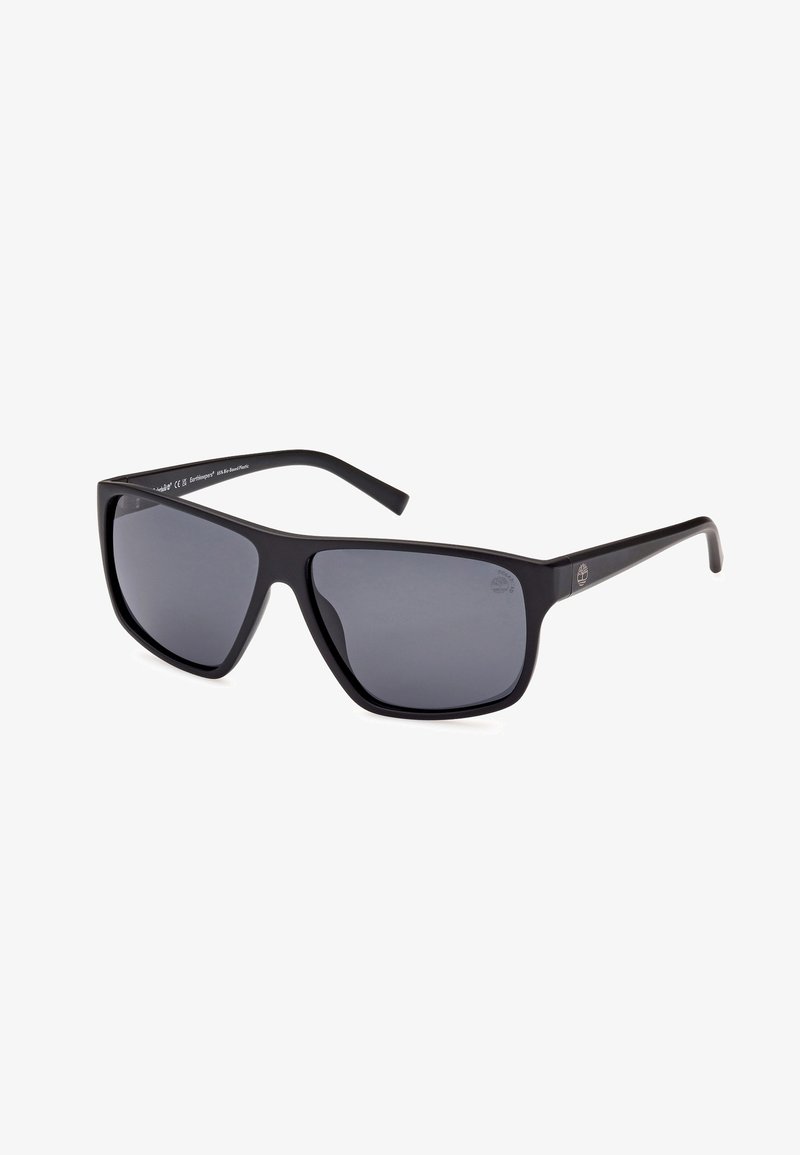 Gafas de sol de plástico negro con lentes gris oscuro, de forma rectangular, con montura ancha y brazos delgados. Presenta el logo en la patilla.