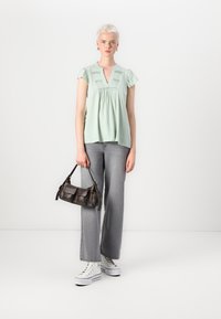 Maglietta verde chiaro con maniche corte a volant e scollatura a V. Abbinata a jeans grigi a gamba larga e sneakers bianche. Borsa scura con più tasche.